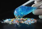 Plava čestica mikroplastike u rukavici iznad hrpe obojanih plastičnih čestica