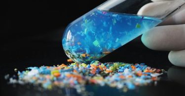 Plava čestica mikroplastike u rukavici iznad hrpe obojanih plastičnih čestica