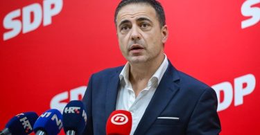 Muškarac u plavom odijelu govori na press konferenciji ispred SDP pozadine
