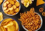 Različite vrste čipsa, fritula i slanog snacka na crnoj površini