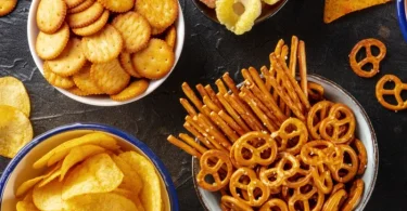 Različite vrste čipsa, fritula i slanog snacka na crnoj površini