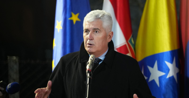 Politički vođa govori na konferenciji sa zastavama u pozadini
