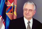Staiji muškarac u odijelu i naočalama pokraj hrvatske zastave