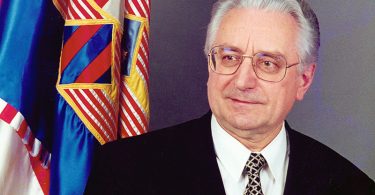 Staiji muškarac u odijelu i naočalama pokraj hrvatske zastave