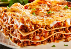 Slojeva lasagna s mjesavinom mesa i rajčice na bijeloj tanjuri, ukrašena svježom petrunjom