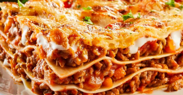 Slojeva lasagna s mjesavinom mesa i rajčice na bijeloj tanjuri, ukrašena svježom petrunjom