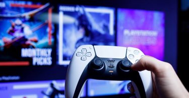 Ruka drži beli PlayStation kontroler sa ekranom u pozadini