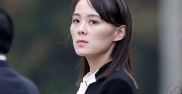 Žena u crnoj odjeći s crvenim značkom, portret u profesionalnom kontekstu