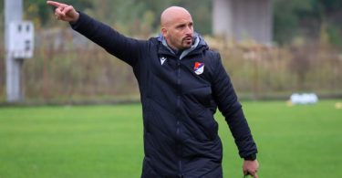 Trener u crnom odijelu daje uputu tijekom utakmice na travnjaku