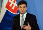Miroslav Lajčak, muškarac u odijelu i kravati, govori pred zastavom, portretna fotografija