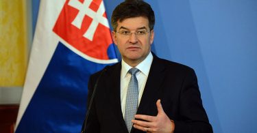 Miroslav Lajčak, muškarac u odijelu i kravati, govori pred zastavom, portretna fotografija