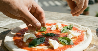 Muškarac priprema Napuljsku pizzu s paradajzom, mocarelom i bosiljkom na drvenoj podlozi