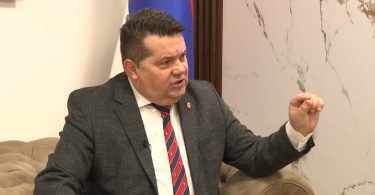 Muškarac u siva odijelu i crvenog kravatom gestikulira tijekom razgovora