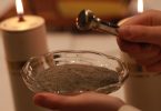 Ruke drže posudu s pepelom tijekom Pepelnice, vatra od svijeće u pozadini