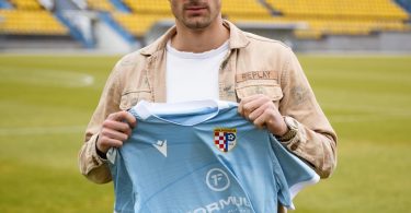 Muškarac u poslovnoj odjeći drži tamnoplavi dres HŠK Posušje na stadionu