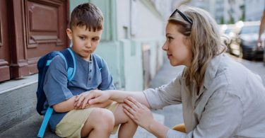 Žena u sivoj majici razgovara s malim dječakom u plavoj košulji na ulici