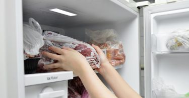 Žena stavlja pakete smrznute hrane u zamrzivač hladnjaka
