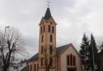 Katolička crkva s crvenom fasadom i crnim tornjem, oznaka mržnje na zidu