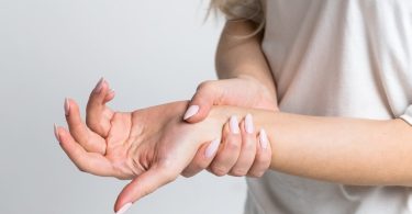 Žena drži zapešće i pokazuje bol ili nelagodu u ruci
