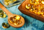 Zlatne kapsule vitamina D u drvenoj žlici i posudi na plavoj površini