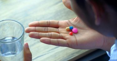 Šaka s različitim dodacima i vitaminima pored čaše vode
