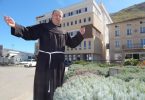 Franjevac u crnoj odjeći s otvorenim rukama ispred zgrade u Mostaru
