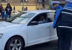 Policajac u plavoj uniformi stoji pored bijelog automobila tokom očevida na ulici
