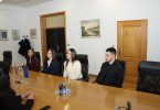 Grupa ljudi u formalnoj odjeći sjeđi za dugim stolom tijekom službene priredbe