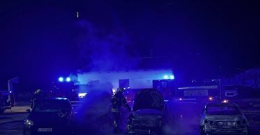 Noćna fotografija više izgorjelih automobila na školskom dvorištu s vozilima hitne pomoći i policije