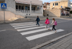 Tri djeteta prelaze cestu na označenom pješačkom prijelazu dok je vozač zaustavljen
