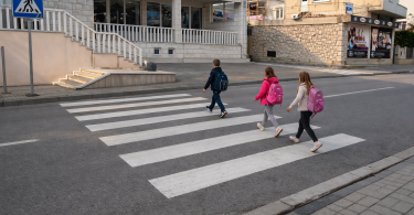 Tri djeteta prelaze cestu na označenom pješačkom prijelazu dok je vozač zaustavljen