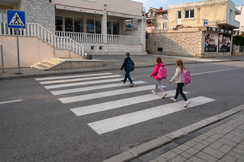 Tri djeteta prelaze cestu na označenom pješačkom prijelazu dok je vozač zaustavljen