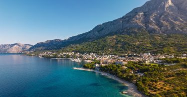 Pogled na obalu Makaarske rivijere s plažom, borovom šumom i планином u pozadini