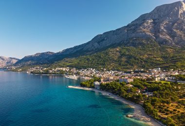 Pogled na obalu Makaarske rivijere s plažom, borovom šumom i планином u pozadini