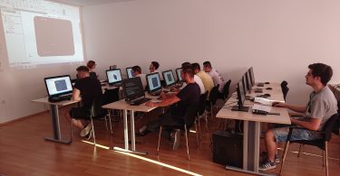 Grupa učesnika sjeduje za računalima tijekom edukativnog treninga u učionici