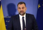 Muškarac u tamnom odijelu i kravati govori na konferenciji s pozadinom zastava BiH i EU