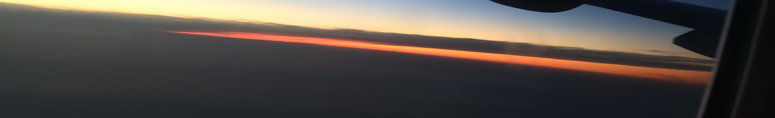 Pogled kroz prozor zrakoplova s krilom tijekom zalaska sunca nad horizontom