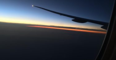 Pogled kroz prozor zrakoplova s krilom tijekom zalaska sunca nad horizontom
