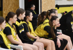 Školske košarkašice u žutim i crnim dresovima sjedavaju na klupi tijekom pripreme za utakmicu
