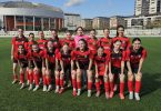 Ženski nogometni tim u crvenim dresovima pozira za timsku fotografiju na travnjaku stadiona
