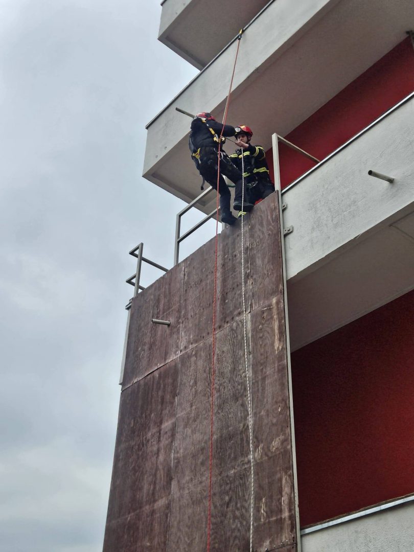 Vatrogasac u uniformi spušta se užetom uz fasadu zgrade tijekom obuke