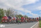 Grupa biciklista u bikelima voze u koloni po asfaltnoj cesti sa zelenilom u pozadini