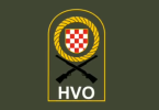 Grb Hrvata s crventim i bijelim poljem u zlatnom krugu s križanim puškama, ispod tekst HVO na vojarskoj podlozi