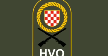 Grb Hrvata s crventim i bijelim poljem u zlatnom krugu s križanim puškama, ispod tekst HVO na vojarskoj podlozi