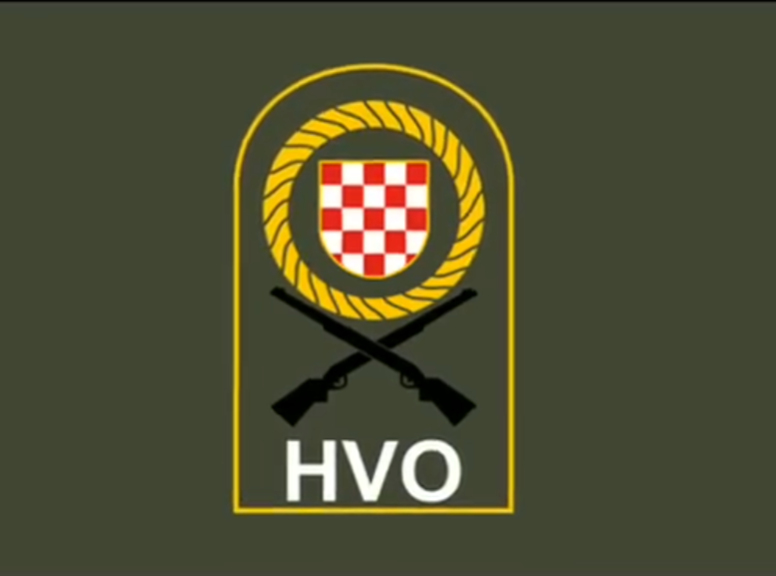 Grb Hrvata s crventim i bijelim poljem u zlatnom krugu s križanim puškama, ispod tekst HVO na vojarskoj podlozi