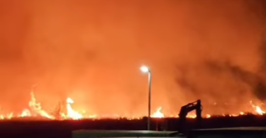 Noćni pogled na široki požar s plamenom i dimom na horizont, rasvjetljeno ulično svjetlo u prvom planu