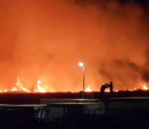 Noćni pogled na široki požar s plamenom i dimom na horizont, rasvjetljeno ulično svjetlo u prvom planu