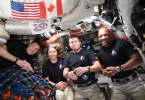 Skupina astronauta u svemirskoj stanici s američkom i kanadskom zastavom u pozadini