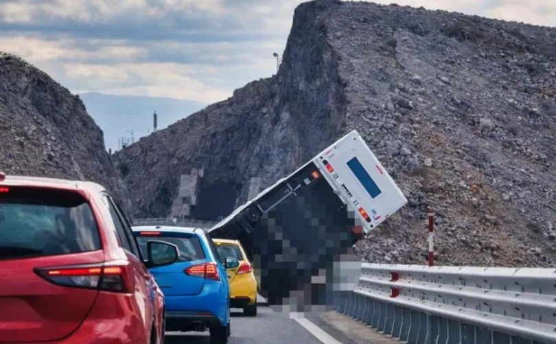 Crveni automobil i prevrnuta bijela prikolica na mostu, stijena u pozadini