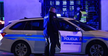 Policijski automobil i policajac tijekom noći ispred zgrade